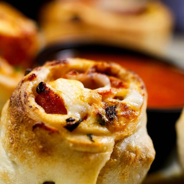 Close-up of golden-brown stuffed pizza rolls with melted cheese and tomato filling on a plate.