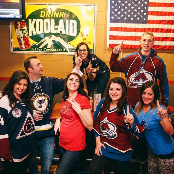 Group of friends in sports jerseys posing in a restaurant booth with an American flag.