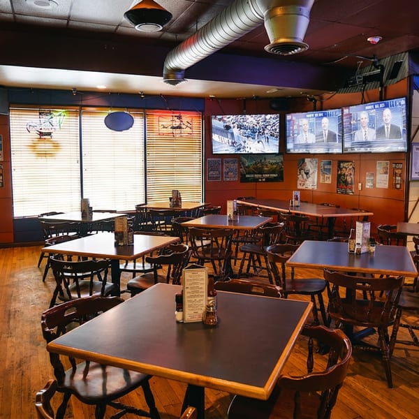 Empty restaurant dining room with wooden tables, chairs, booths, and multiple TVs showing sports.