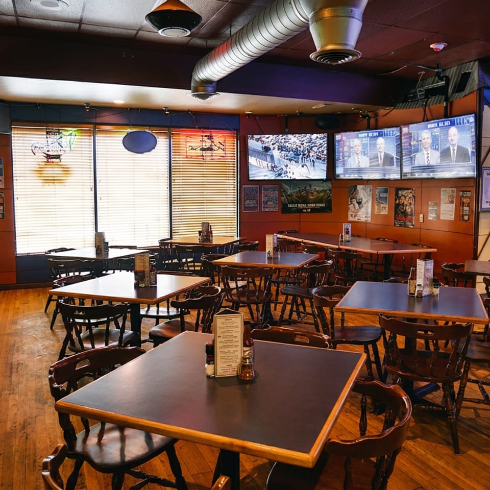 Empty restaurant dining room with wooden tables, chairs, booths, and multiple TVs showing sports.