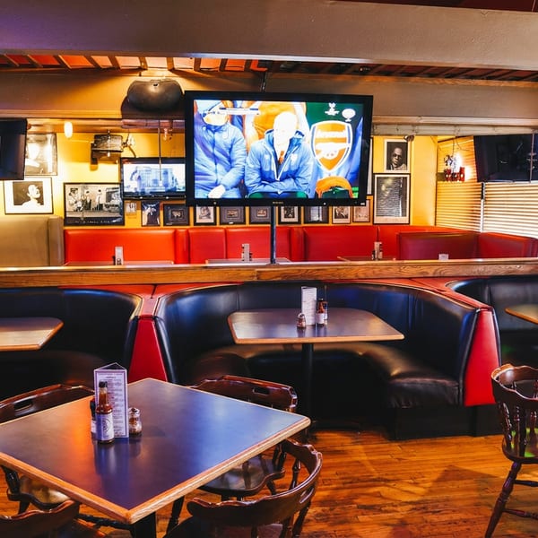 Cozy restaurant interior with black booths, wooden tables, and multiple TVs showing sports.