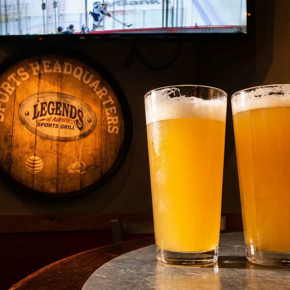 Two beers on a table with a Legends Sports Grill barrel sign and hockey game on TV.