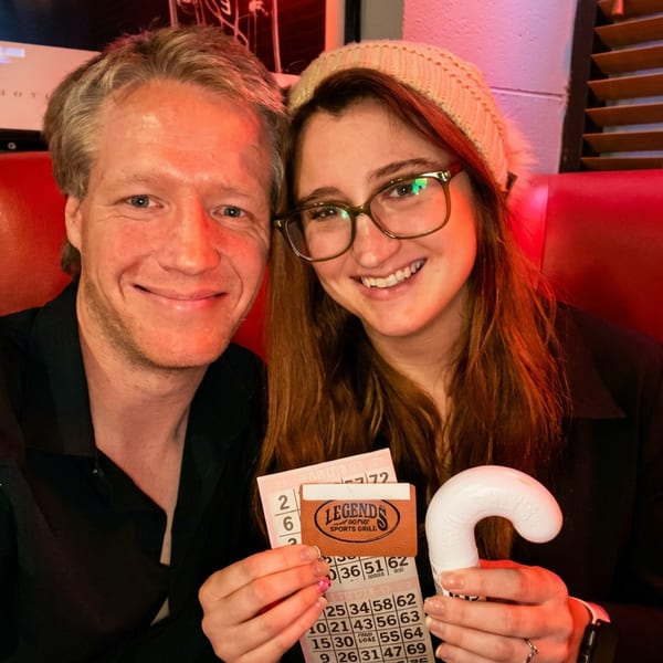 A smiling couple in a red booth holds bingo cards and a Legends Sports Grill gift card.