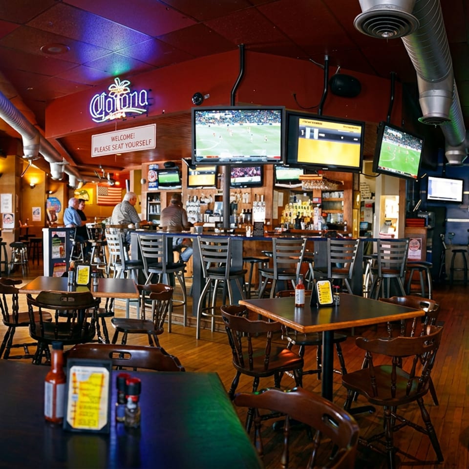 A lively sports bar interior with multiple TVs showing games, a full bar, and dining tables.